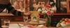 Hand placing a Golden Child fresh dog food pouch on a dinner table set with flowers and fruit
