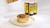 Bowl of fresh dog food topped with gravy beside three Golden Child drizzle dog food toppers